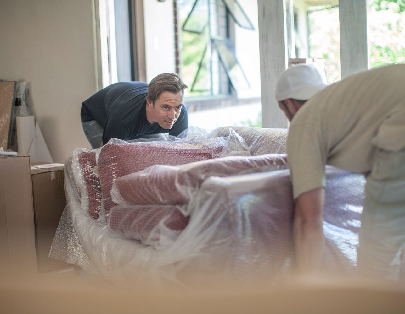 Two movers carrying a wrapped couch into a home
