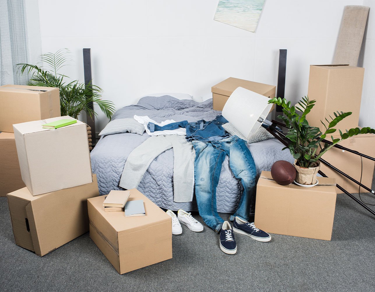 Moving boxes and folded clothes piled on a bed in a partially packed room