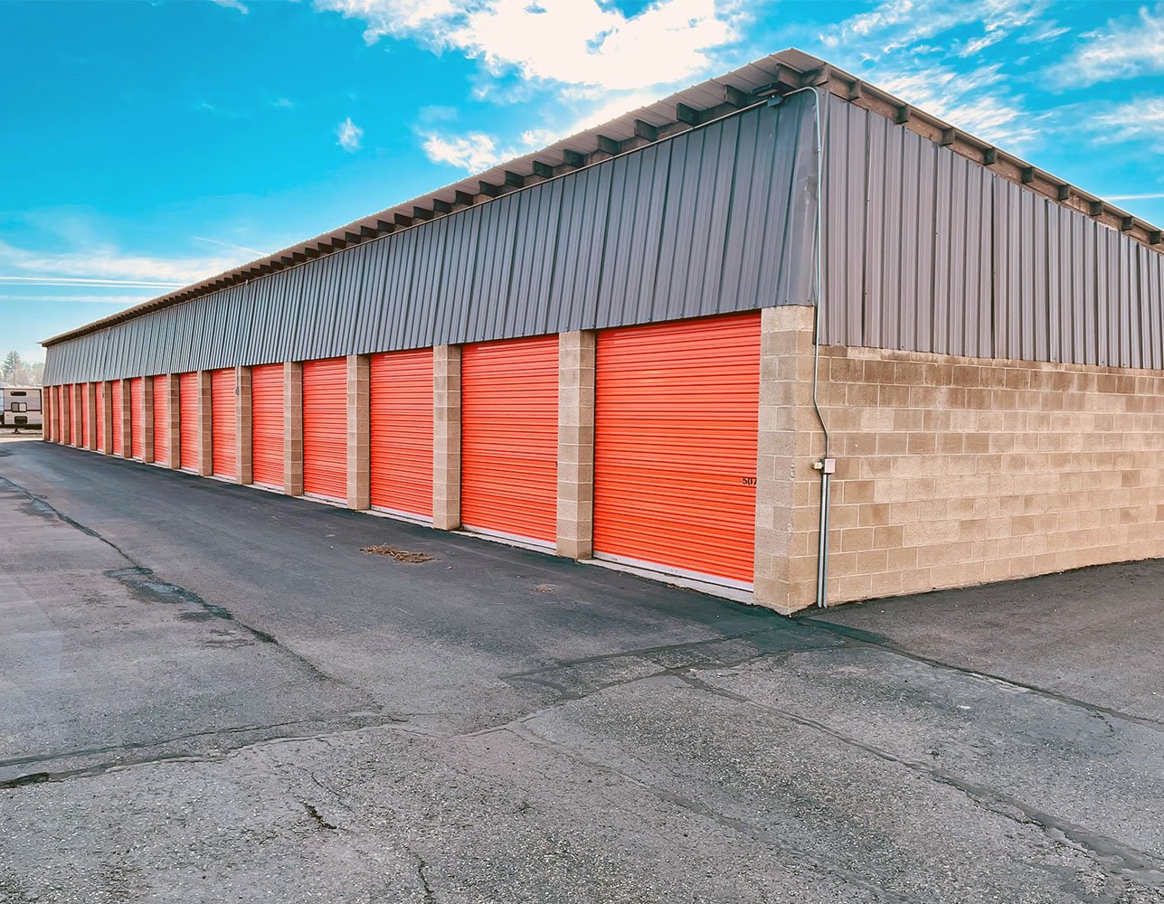 Exterior of a self-storage facility with red roll-up doors under a blue sky